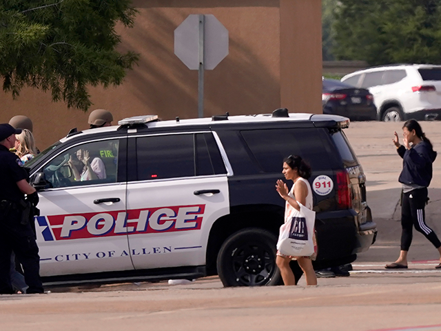 People raise their hands as they leave a shopping center after a shooting, Saturday, May 6