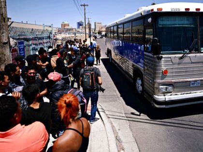 A bus drives past migrants as they wait to turn themselves in to US Customs and Border Pro