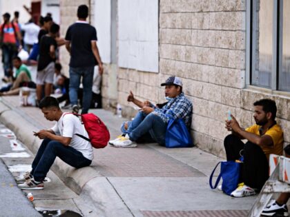 Migrants that arrived from Mexico look at their phones as they wait for transportation nea