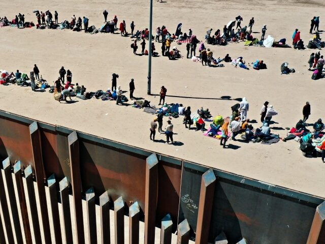 An aerial image shows migrants waiting along the border wall to surrender to Border Patrol