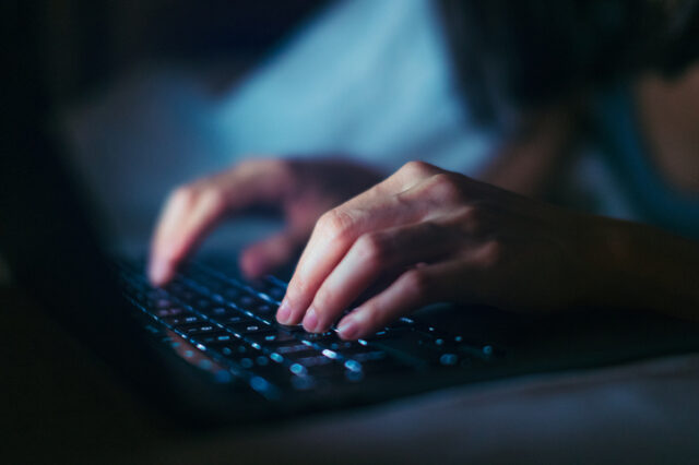 Close-up shot of female hands typing on computer keyboard, lying on bed, working late at h