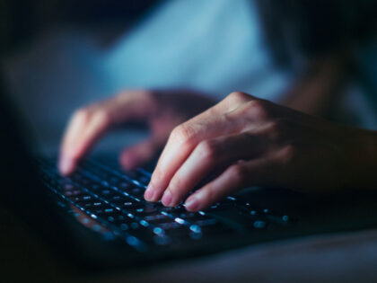 Close-up shot of female hands typing on computer keyboard, lying on bed, working late at home.