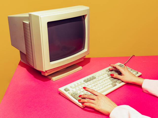 Colorful image of vintage computer monitor and keyboard on bright pink tablecloth over yel