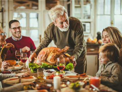 Happy mature man talking to his grandchild while bringing Thanksgiving turkey to the table.