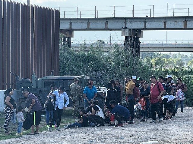 A group of migrants walk around the end of the Texas-built border wall to surrender to law