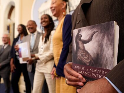 FILE — Dr. Amos C. Brown, Jr., vice chair for the California Reparations Task Force, right, holds a copy of the book Songs of Slavery and Emancipation, as he and other members of the task force pose for photos at the Capitol in Sacramento, Calif., on June 16, 2022. Economists …