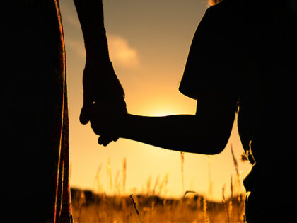Silhouette of mother and child holding hands facing the sunset. - stock photo