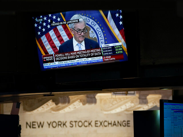 A display shows Fed Chairman Jerome Powell's news conference while traders work on th