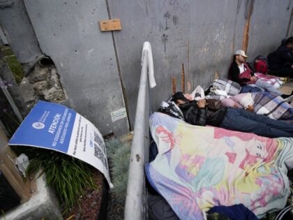People waiting to apply for asylum sleep in front or a sign for the CBP One app as they camp near the pedestrian entrance to the San Isidro Port of Entry, linking Tijuana, Mexico with San Diego, Thursday, June 1, 2023, in Tijuana, Mexico. U.S. authorities raised the number of …