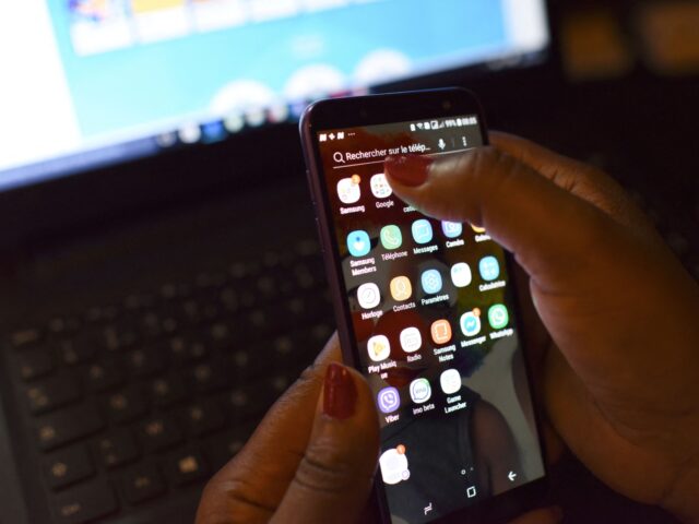 A woman uses a smartphone in front of a laptop on April 3, 2019, in Abidjan. - According to the figures of the platform of the fight against cybercrime (PLCC) of the national police, nearly one hundred crooks of the internet, were arrested in 2018 in Ivory Coast, a country …