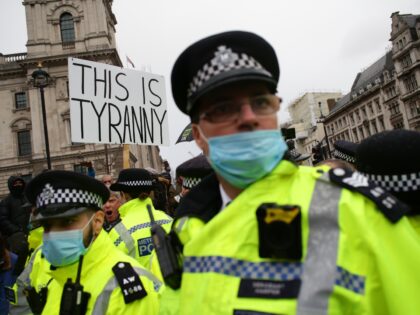 An activist protesting against coronavirus lockdown restrictions and any mandated covid-19 vaccinations holds a placard reading 'This Is Tyranny' above police officers in Parliament Square in London, England, on December 14, 2020. London is expected to be imminently placed under 'Tier 3' restrictions, indicating a 'very high' coronavirus alert level, …