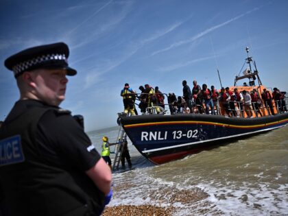 TOPSHOT - A British police officer stands guard on the beach of Dungeness, on the southeast coast of England, on June 15, 2022, as Royal National Lifeboat Institution's (RNLI) members of staff help migrants to disembark from one of their lifeboat after they were picked up at sea while attempting …