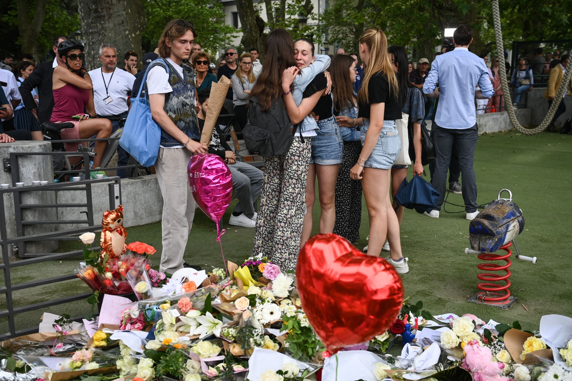 People hug in front of flowers and candles for the victims of a stabbing attack that occured the day before in the 'Jardins de l'Europe' parc in Annecy, French Alps, on June 9, 2023. A man armed with a knife stabbed four preschool children and injured two adults by a lake in the French Alps on June 8 in an attack that sent shock waves through the country. The suspect is a Syrian in his early 30s who was granted refugee status in Sweden in April, a police source told AFP. He was arrested at the scene. (Photo by OLIVIER CHASSIGNOLE / AFP) (Photo by OLIVIER CHASSIGNOLE/AFP via Getty Images)