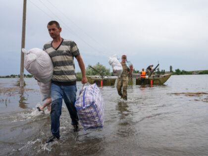 Local residents carry belongings from a boat during the evacuation of a flooded area in Afanasiyivka, Mykolayiv region on June 10, 2023, following damages sustained at Kakhovka hydroelectric power plant dam. (Photo by Oleksii Filippov / AFP) (Photo by OLEKSII FILIPPOV/AFP via Getty Images)