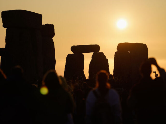 The sun rises behind the stone circle as people gather to take part in the Summer Solstice