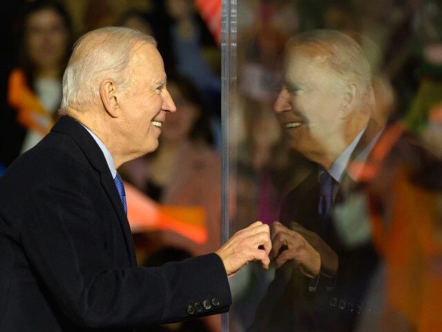 US President Joe Biden peers around a protective bullet=proof screen during a celebration