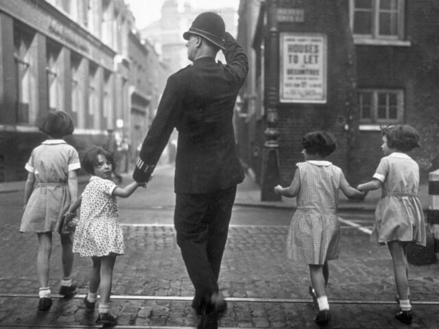 28th August 1934: A group of children crossing Rosebery Avenue , London under the watchfu