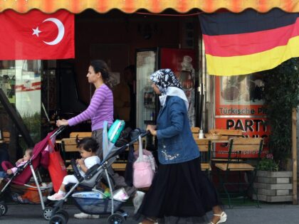 BERLIN - JUNE 23: A Muslim woman wearing a headscarf pushes a pram past German and Turkish flags fluttering from the awning of a cafe in the immigrant-heavy district of Wedding two days ahead of the Germany vs. Turkey Euro 2008 semi-finals football match on June 23, 2008 in Berlin, …