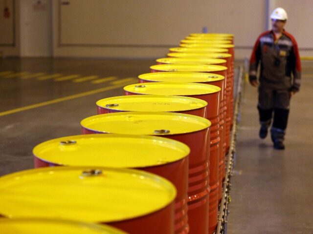 An employee walks past a conveyor belt carrying barrels of lubricant oil at Royal Dutch Sh