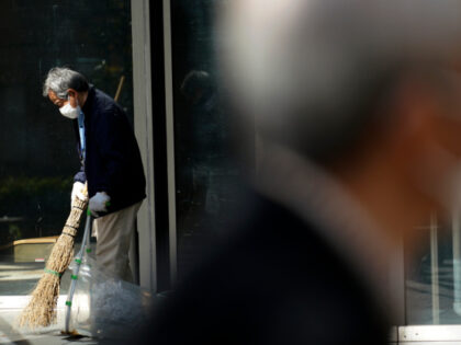 A man wearing a protective face mask sweeps the entrance to a building Thursday, April 2,