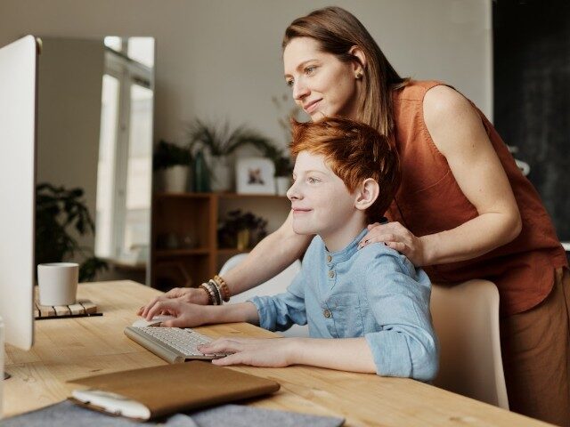 A mother looks over her son's shoulder as he works on the computer (Pexels/Julia M. Camero
