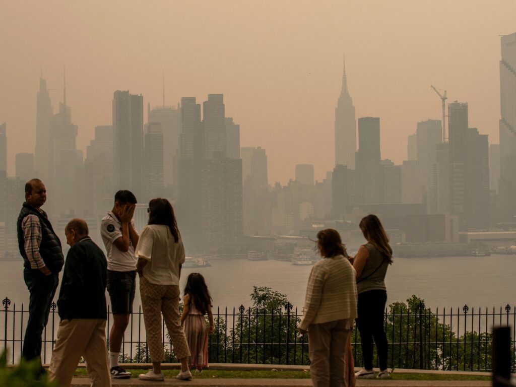 WEEHAWKEN, NEW JERSEY - JUNE 7: People stand in a park as the New York City skyline is covered with haze and smoke from Canada wildfires on June 7, 2023 in Weehawken, New Jersey. Air pollution alerts were issued across the United States due to smoke from wildfires that have been burning in Canada for weeks. (Photo by Eduardo Munoz Alvarez/Getty Images)