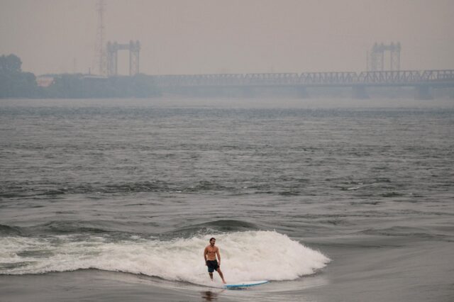 A man surfs in the St. Lawrence river with smoke caused by wildfires in northern Quebec in