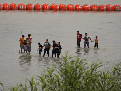 Migrants who crossed the Rio Grande from Mexico walk past large buoys being deployed as a