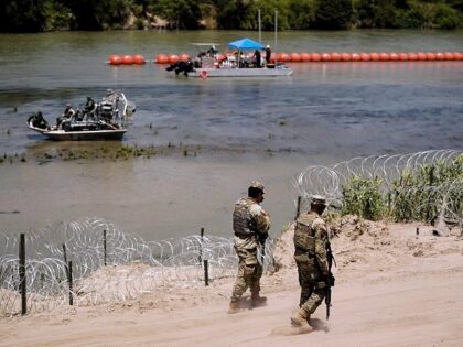 Guardsmen patrol as workers continue to deploy large buoys to be used as a border barrier along the banks of the Rio Grande in Eagle Pass, Texas, Wednesday, July 12, 2023. The floating barrier is being deployed in an effort to block migrants from entering Texas from Mexico. (AP Photo/Eric …