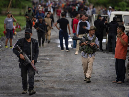 Armed Meitei community members carry automatic weapons as they rush towards a hillock wher