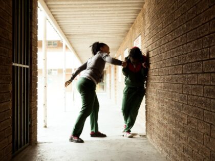 A school girl bullies another girl in a secluded passageway outside a school building. Alm