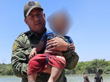 A Border Patrol agent carries a severely dehydrated migrant child rescued from the bank of