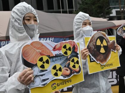 TOPSHOT - South Korean environmental activists wearing protective clothing and a mask (R) of Japan's Prime Minister Yoshihide Suga hold pictures of fishes with radioactivity warning signs during a protest against Japan's decision on releasing Fukushima wastewater, near the Japanese embassy in Seoul on April 13, 2021. (Photo by Jung …