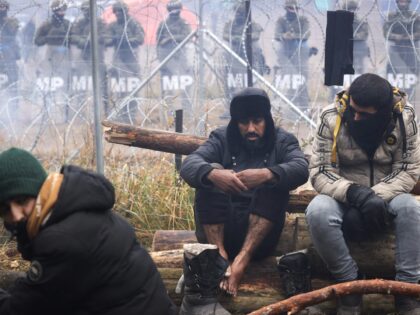 TOPSHOT - Poland's servicemen stand behind a barbed wire fence on the Belarusian-Polish border as migrants warm at the fire, on the Belarusian side in the Grodno region on November 14, 2021. - Dozens of migrants have been detained after crossing into Poland from Belarus, Warsaw said on November 14, …