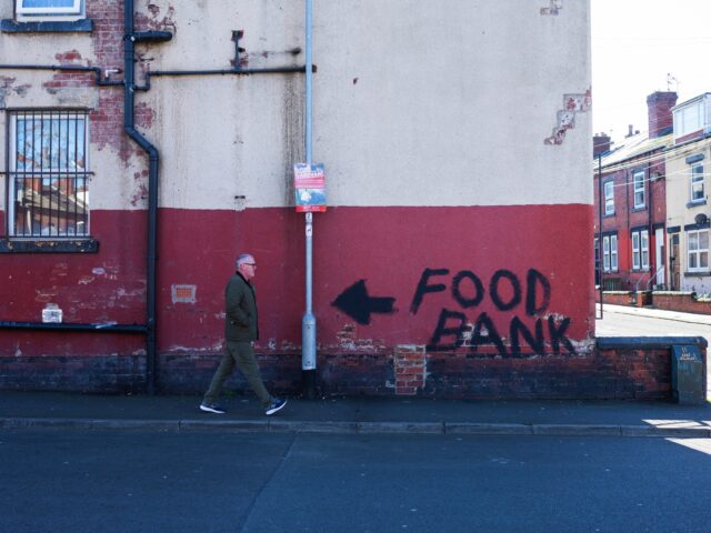 A man walks past a terraced house, the walls of which bare graffiti reading "food bank" an