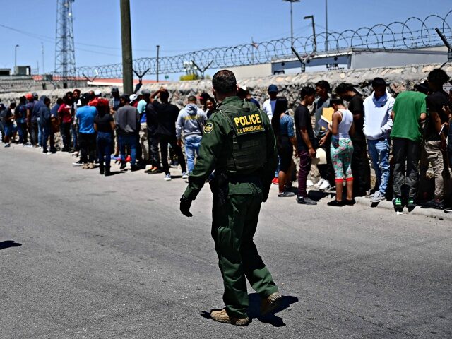 Border Patrol agents walk along a line of migrants waiting to turn themselves in to US Cus