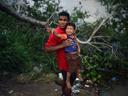 TOPSHOT - A migrant carrying a child tries to get to the US through the Rio Grande River a