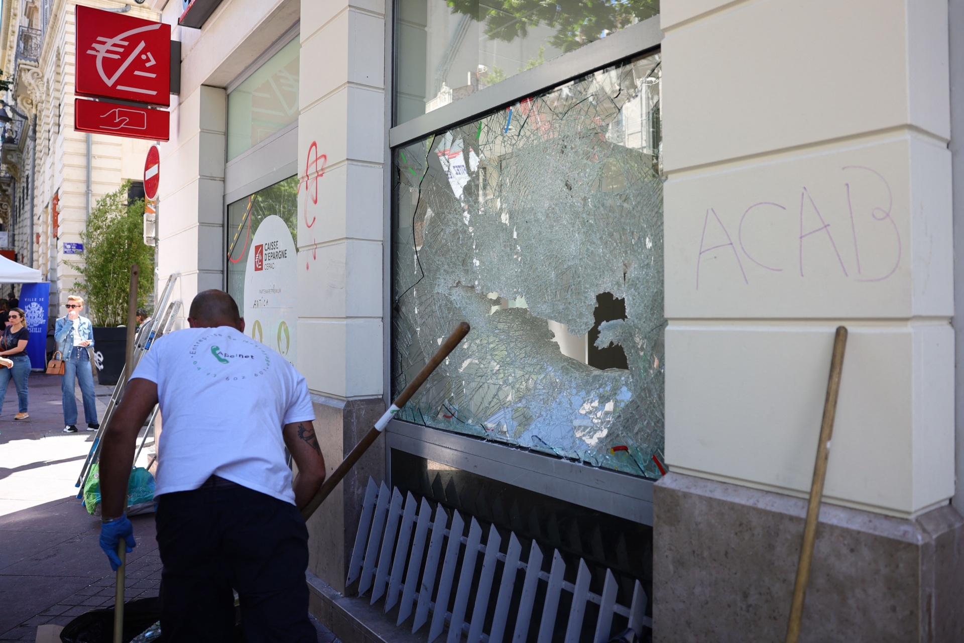 A cleaning contractor cleans debris next to a damaged window of a Caisse d'Epargne bank in the centre of Marseille, southern France on July 1, 2023, after a fourth consecutive night of rioting in France over the killing of a teenager by police. French police arrested 994 people nationwide during a fourth consecutive night of rioting over the killing of a teenager by police, the interior ministry said on July 1, 2023. France had deployed 45,000 officers overnight backed by light armoured vehicles and crack police units to quell the violence over the death of 17-year-old Nahel, killed during a traffic stop in a Paris suburb on June 27, 2023. (Photo by CLEMENT MAHOUDEAU / AFP) (Photo by CLEMENT MAHOUDEAU/AFP via Getty Images)