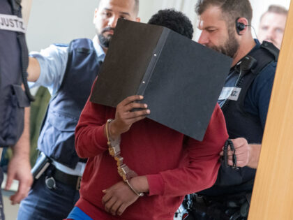 04 July 2023, Baden-Württemberg, Ulm: The handcuffed defendant (M), who covers his face with a file folder, is led by court officials into the hearing room of the Regional Court. The asylum seeker from Eritrea was sentenced to life imprisonment in the case of the knife attack on two schoolgirls …