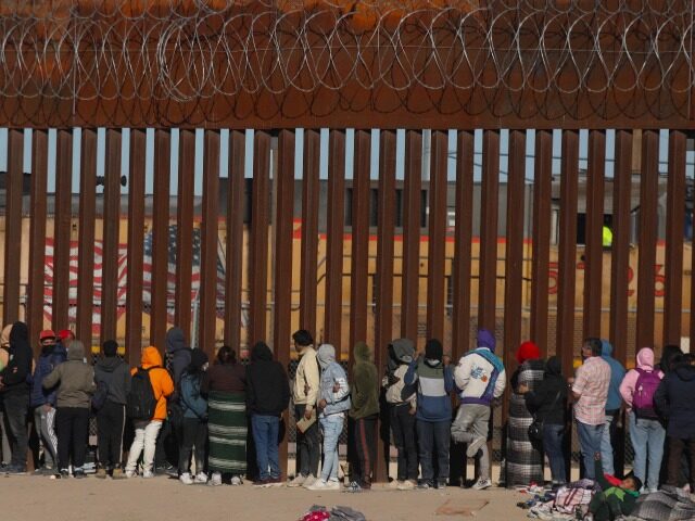 Migrants queue at the border wall to be received by Border Patrol agents after crossing th