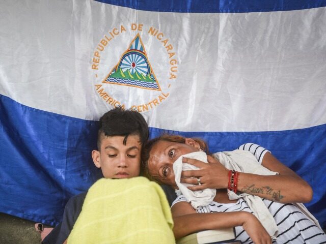 Migrants taking part in a caravan heading to the US, rest against a wall with a Nicaraguan
