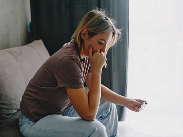 A young woman holds a device reading a pregnancy test. - stock photo