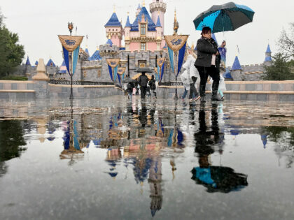 sANAHEIM, CA - MARCH 12: Disneyland guests walk past the Sleeping Beauty Castle while visiting Disneyland amid rain showers in Anaheim, Calif., on March 12, 2020. Disneyland will temporary close the Disneyland Resort in Anaheim in response to the expanding threat posed by the Coronavirus Pandemic. The closure takes effect …