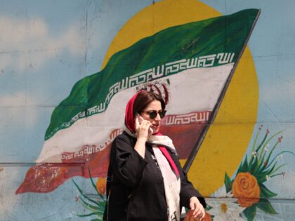 An Iranian woman walks past an Iranian flag painted on a wall in a street in Tehran on Apr