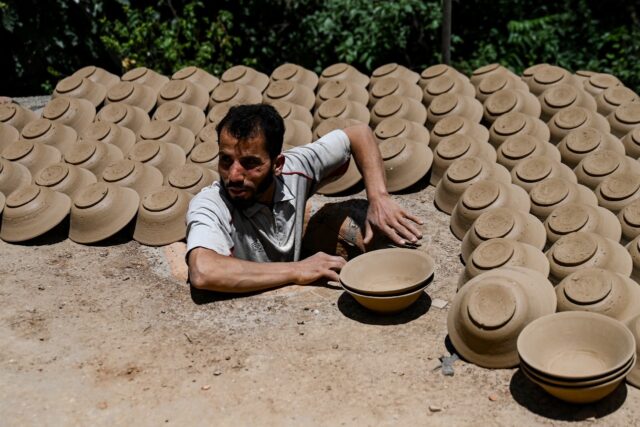 An Afghan potter takes sun-dried bowls from the roof of his kiln to stack for firing in Is