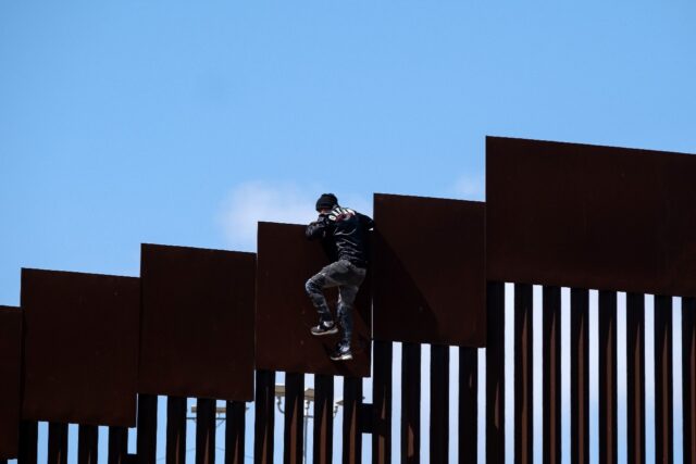 A migrant scales the border fence near Tijuana, Mexico, to enter the United States in May