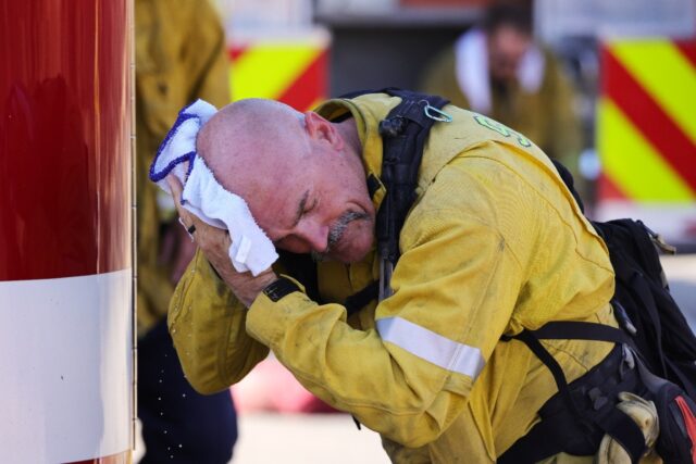A San Bernardino County firefighter wipes his head as the Oak Fire burns near Fontana, Cal