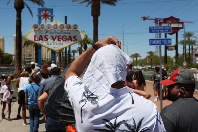A man shields himself from the sun while waiting in line to take a photo at the historic W
