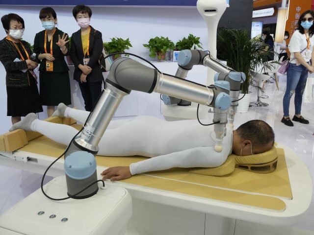 Visitors look at robot arms performing acupressure massage at a booth during China Interna