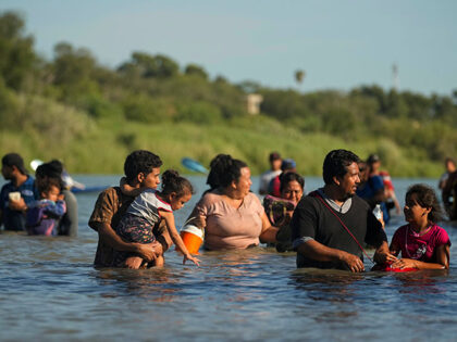 Migrants navigate around concertina wire along the banks of the Rio Grande after crossing